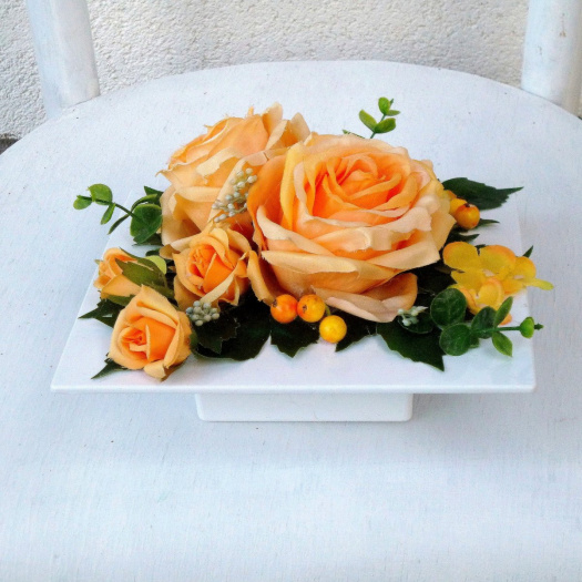 Aranžmá se žluto oranžovými růžemi a hortenzií na bílé misce