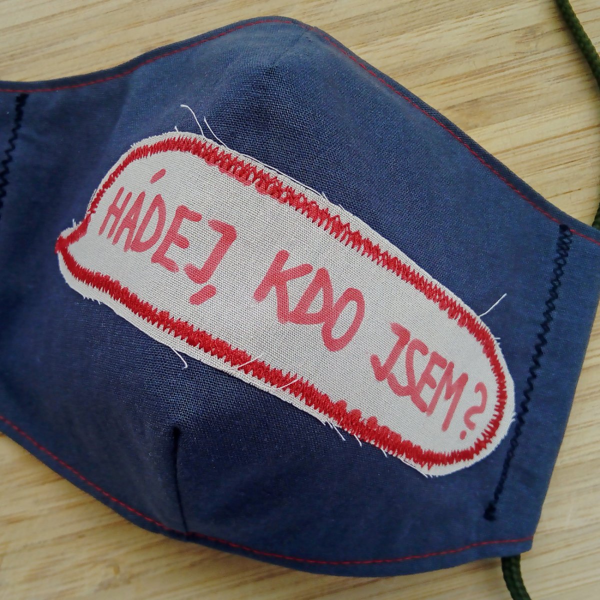 Šedá rouška s nápisem Hádej, kdo jsem?